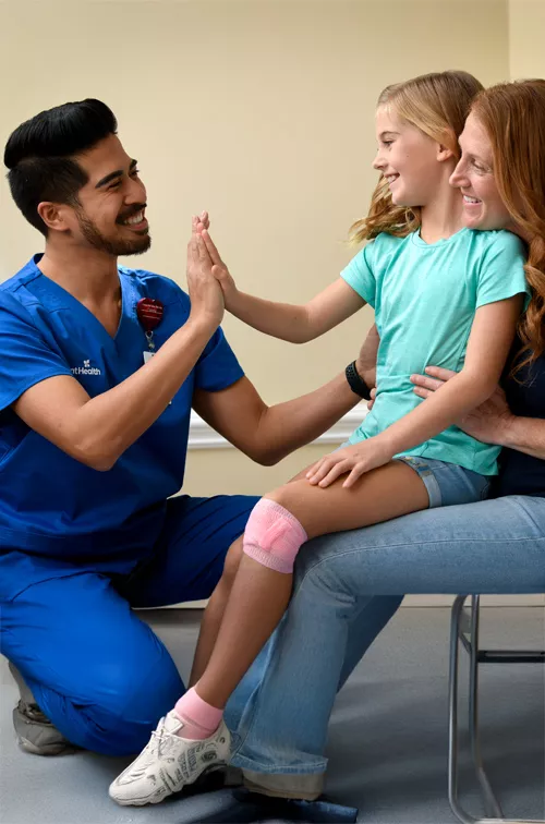 A Child Patient Sits in Her Mother's Lap While a Physician High Fives Her