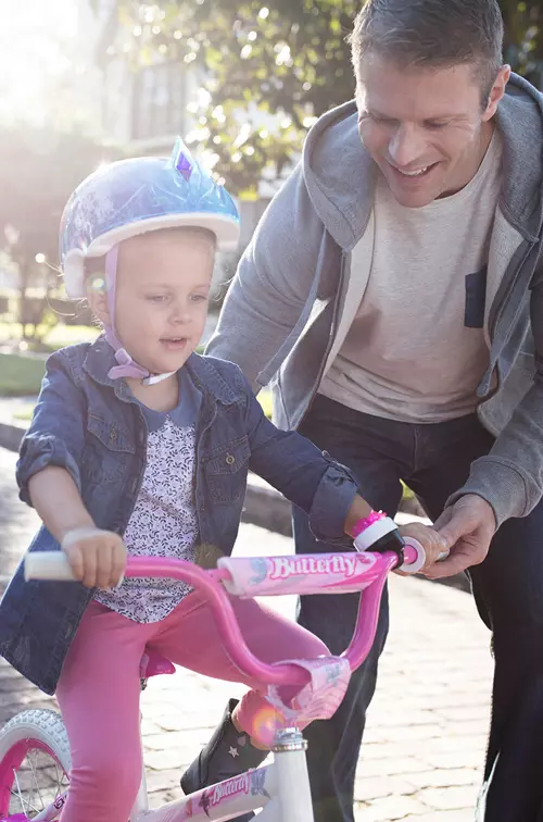 Father teaching his young daughter how to ride a pink bike in the street.