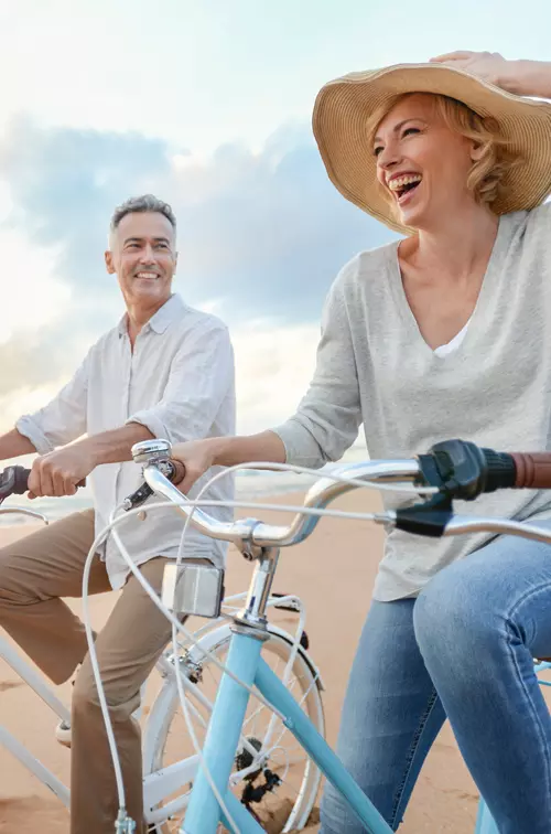 Man and woman in a hat riding bicycles on the beach at sunset. 