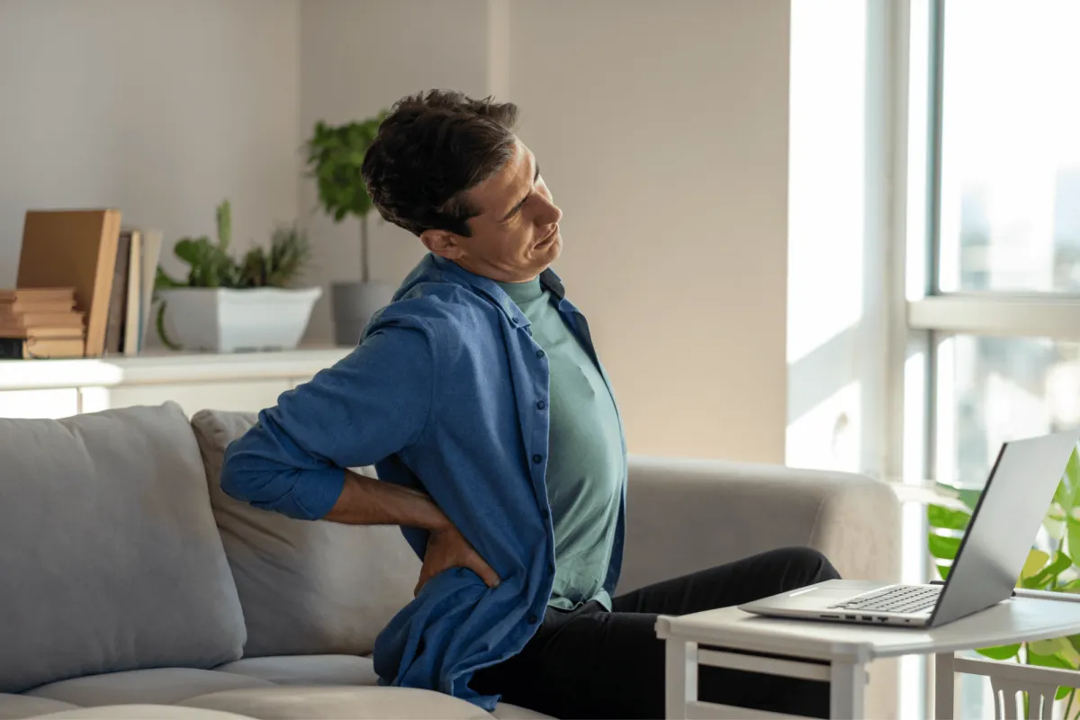 Man sitting on sofa in living room with back pain trying to ease tension