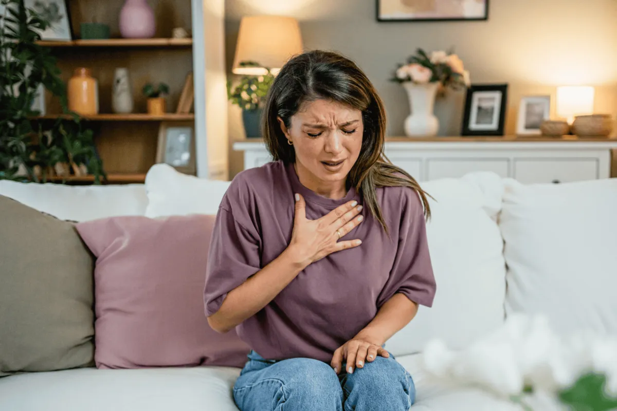 Woman Sitting on her couch clutching her chest with pain